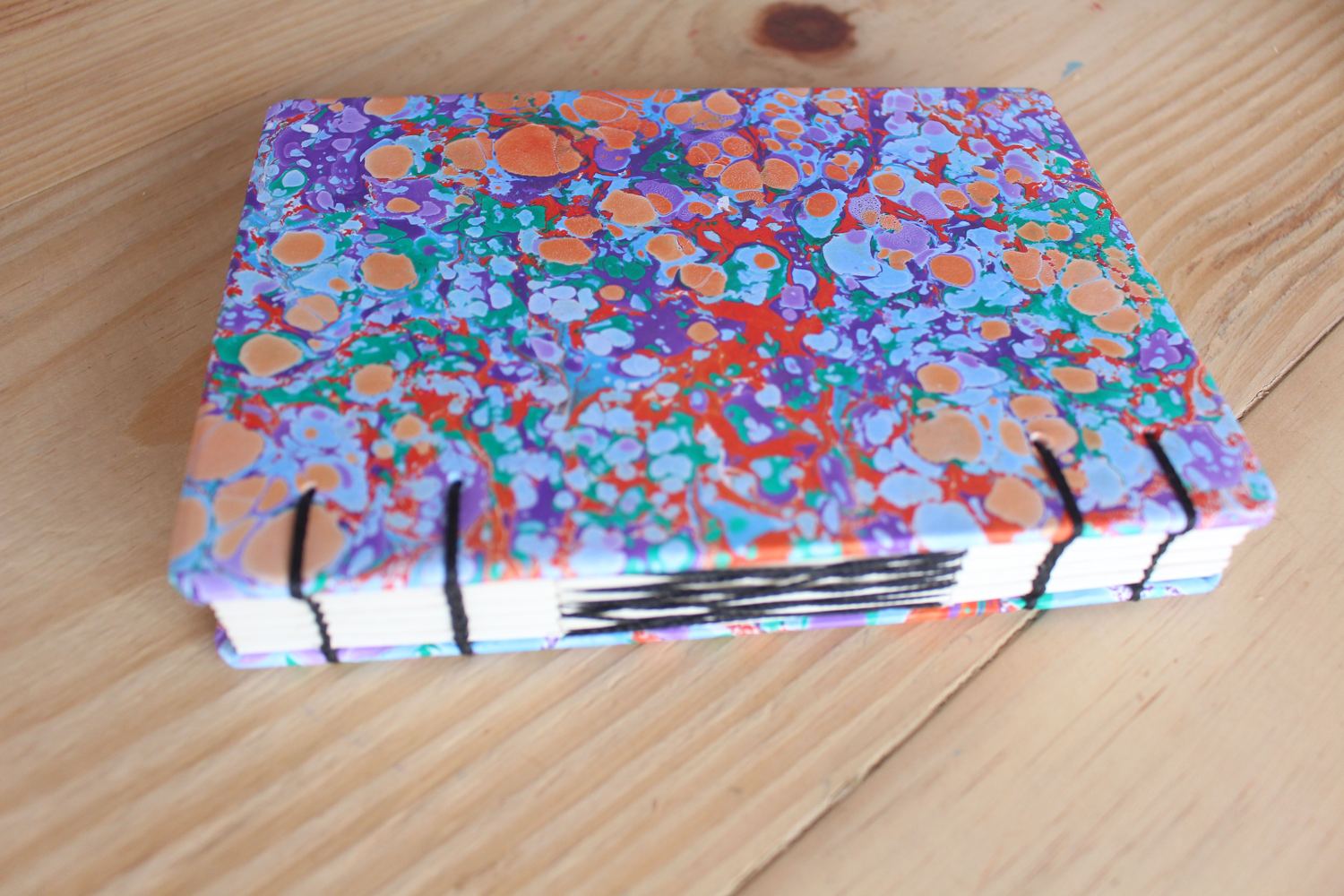 Caderno artesanal com capa marmorizada e costura copta aparente, feito no ateliê da Feitio Arte